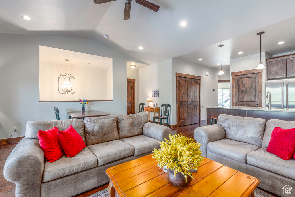 Living room with wood finished floors, ceiling fan with notable chandelier, baseboards, lofted ceiling, and recessed lighting