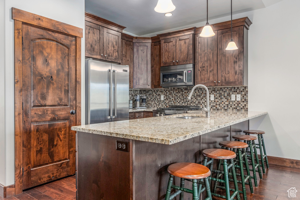 Kitchen featuring a peninsula, baseboards, appliances with stainless steel finishes, and dark wood-type flooring