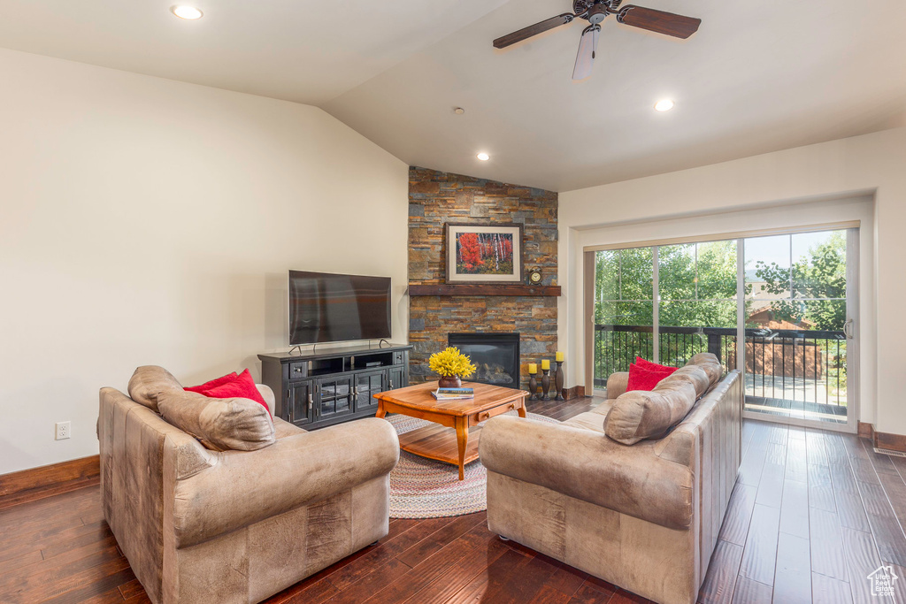 Living room with vaulted ceiling, a stone fireplace, ceiling fan, and dark wood finished floors