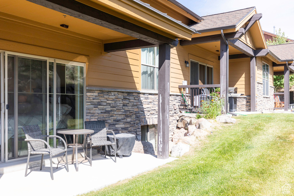 Exterior space featuring a lawn, roof with shingles, stone siding, and a patio