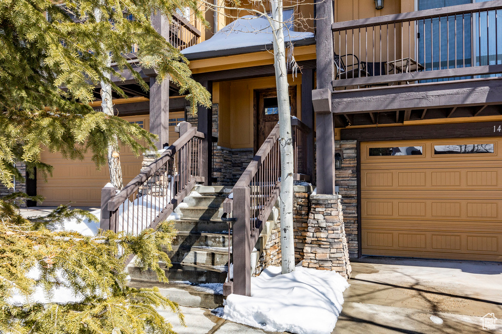 View of exterior entry with stone siding, a balcony, and a garage
