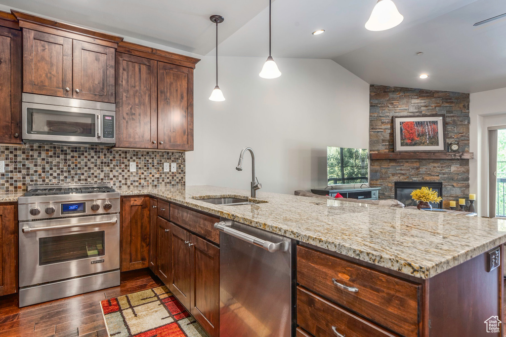 Kitchen with appliances with stainless steel finishes, a sink, vaulted ceiling, dark wood-type flooring, and a peninsula