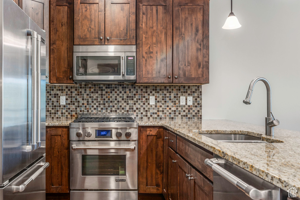 Kitchen featuring high quality appliances, a sink, light stone countertops, backsplash, and dark brown cabinets