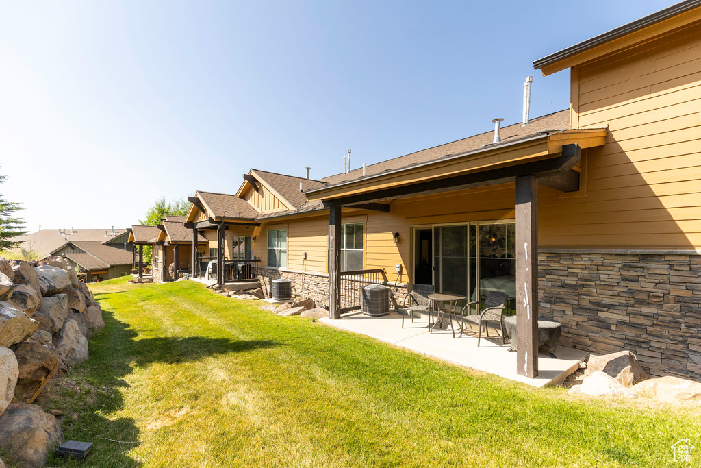 Rear view of house featuring stone siding, a lawn, central AC unit, and a patio