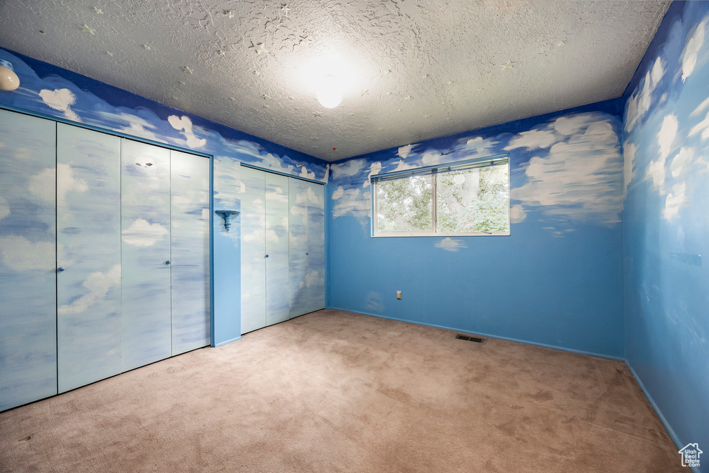 Unfurnished bedroom with multiple closets, carpet, and a textured ceiling