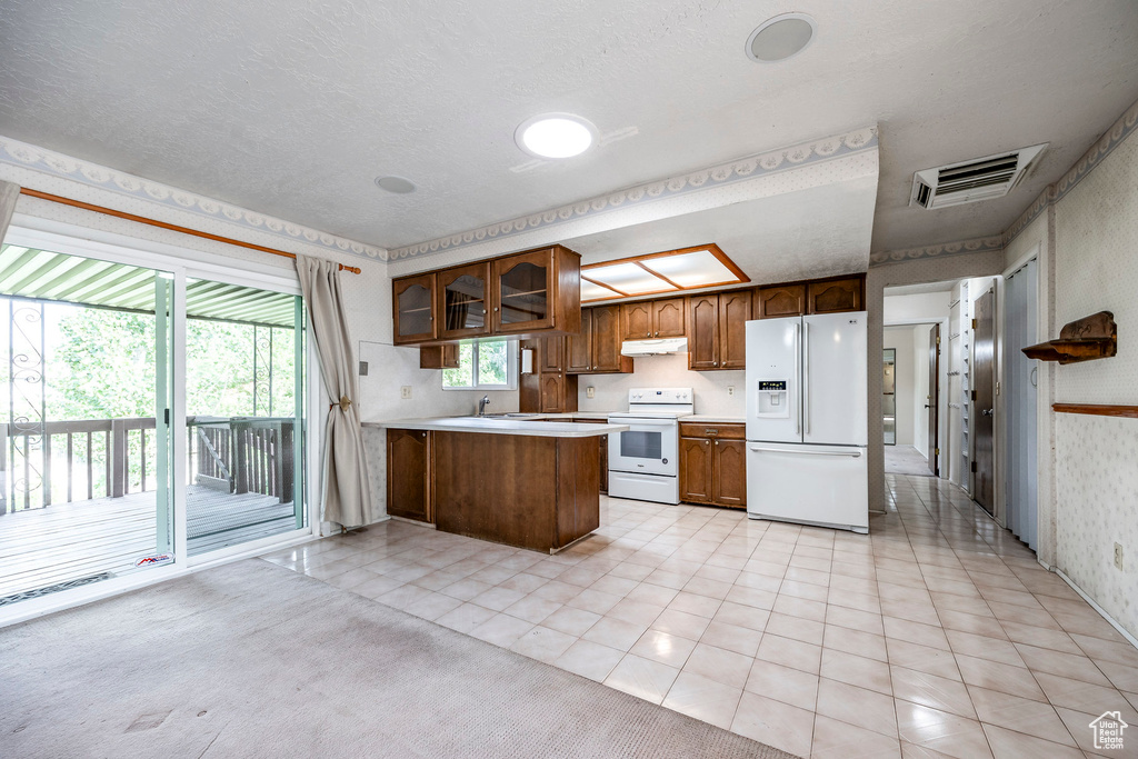 Kitchen with white appliances, light carpet, sink, a textured ceiling, and kitchen peninsula