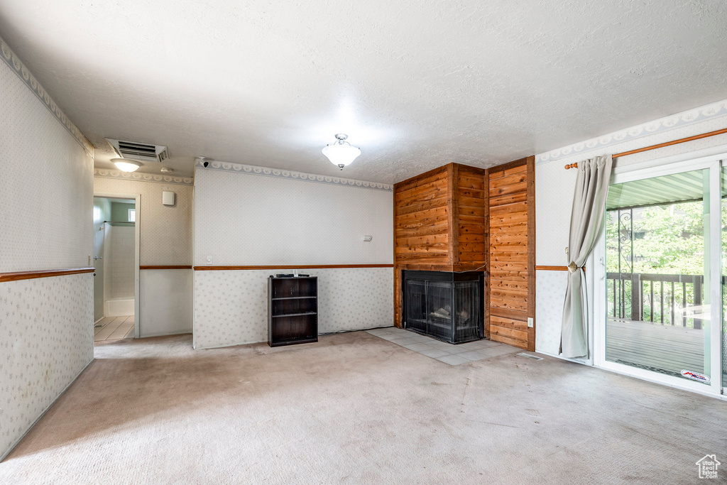 Unfurnished living room with a textured ceiling, a multi sided fireplace, wooden walls, and light colored carpet