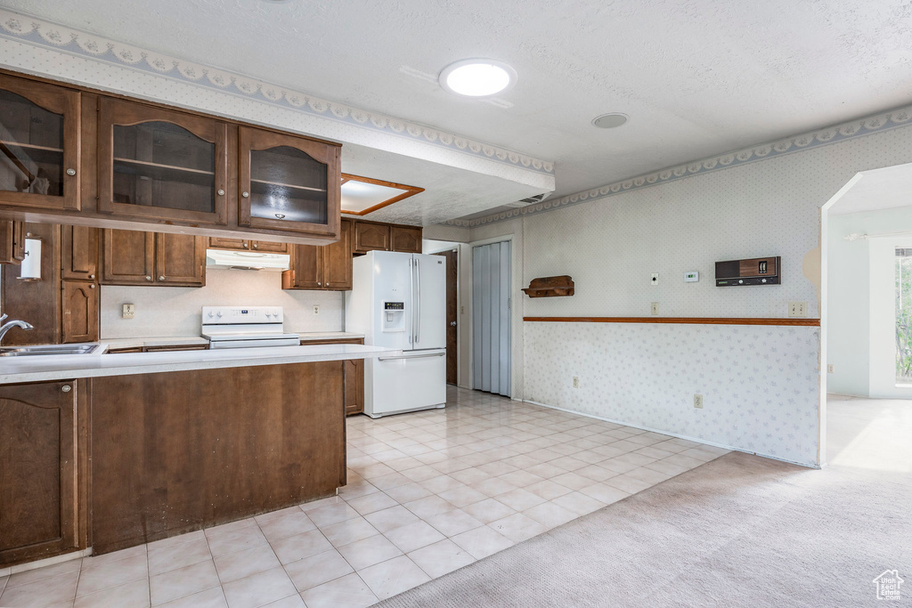 Kitchen with white appliances, a textured ceiling, light colored carpet, dark brown cabinetry, and sink