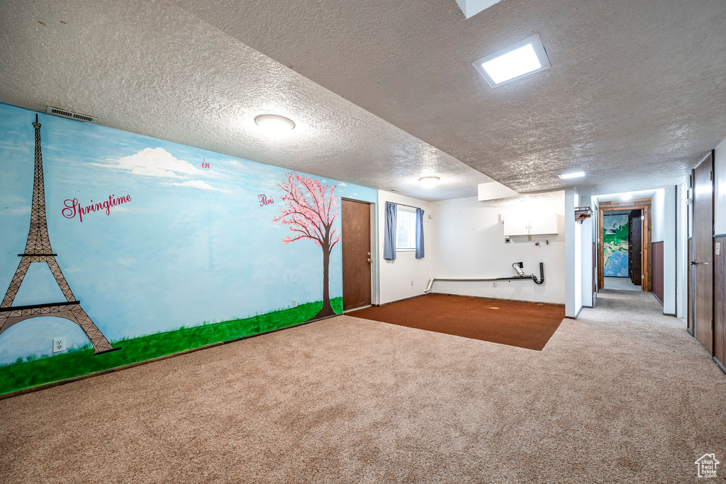 Basement featuring light colored carpet and a textured ceiling