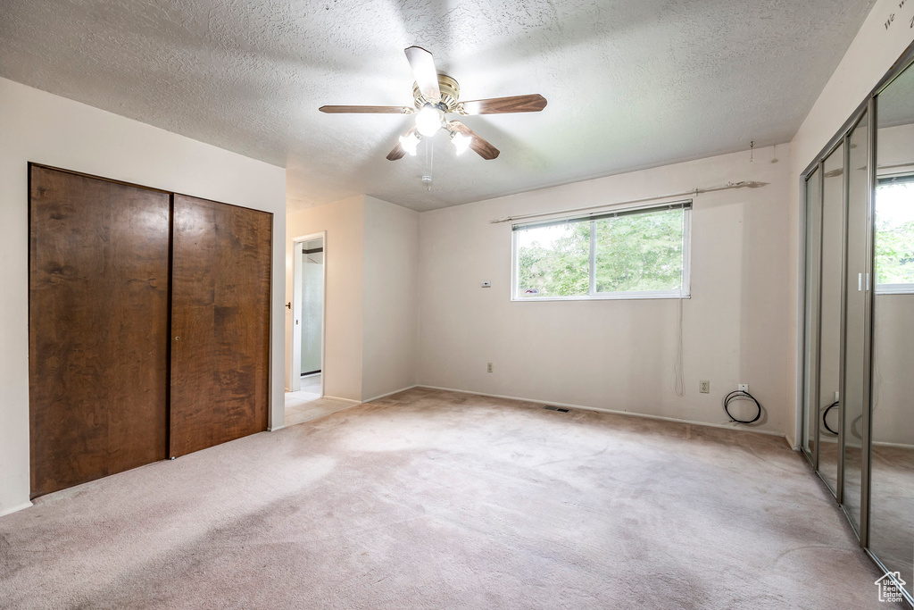 Unfurnished bedroom with multiple windows, light carpet, ceiling fan, and a textured ceiling