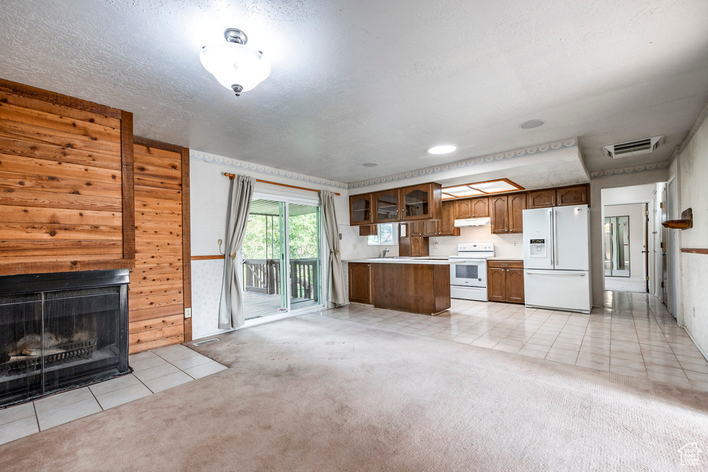 Kitchen with wood walls, light carpet, white appliances, and a textured ceiling