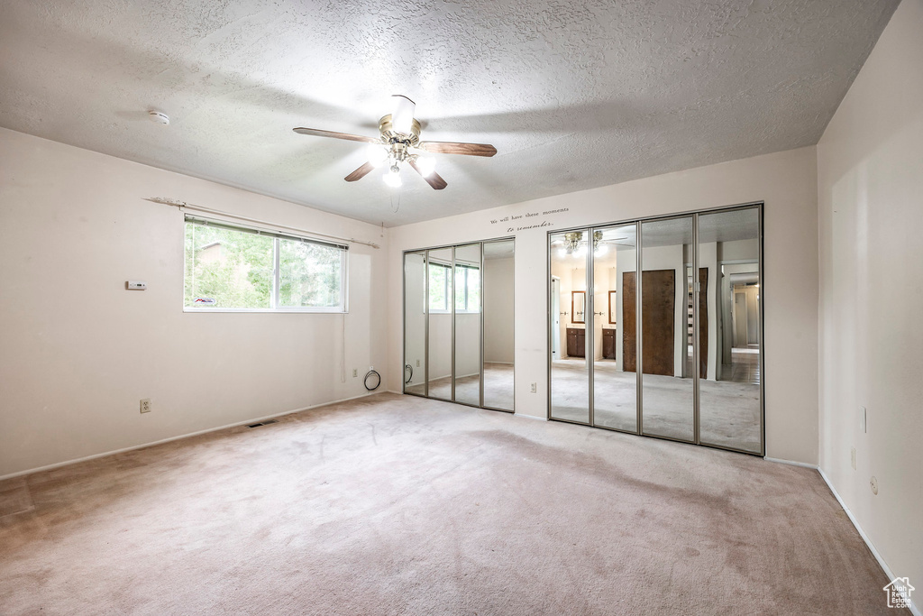 Unfurnished bedroom featuring multiple closets, light carpet, a textured ceiling, and ceiling fan