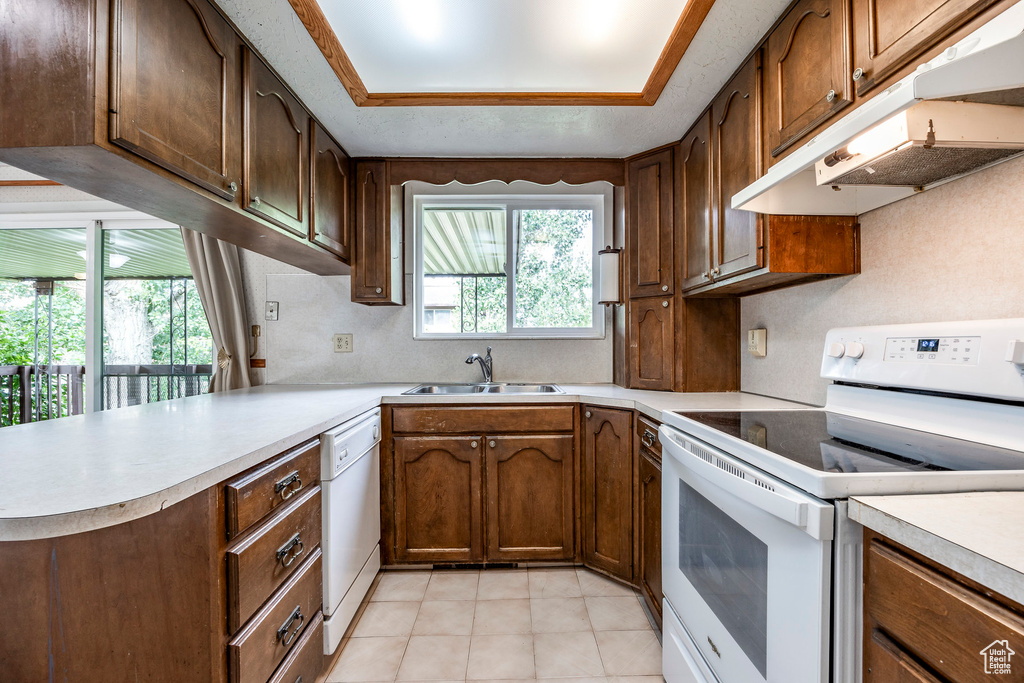 Kitchen with white appliances, sink, kitchen peninsula, light tile patterned floors, and a tray ceiling