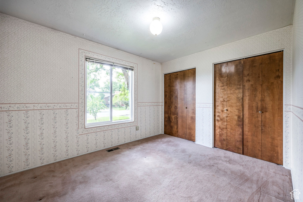 Unfurnished bedroom with a textured ceiling, carpet floors, and two closets