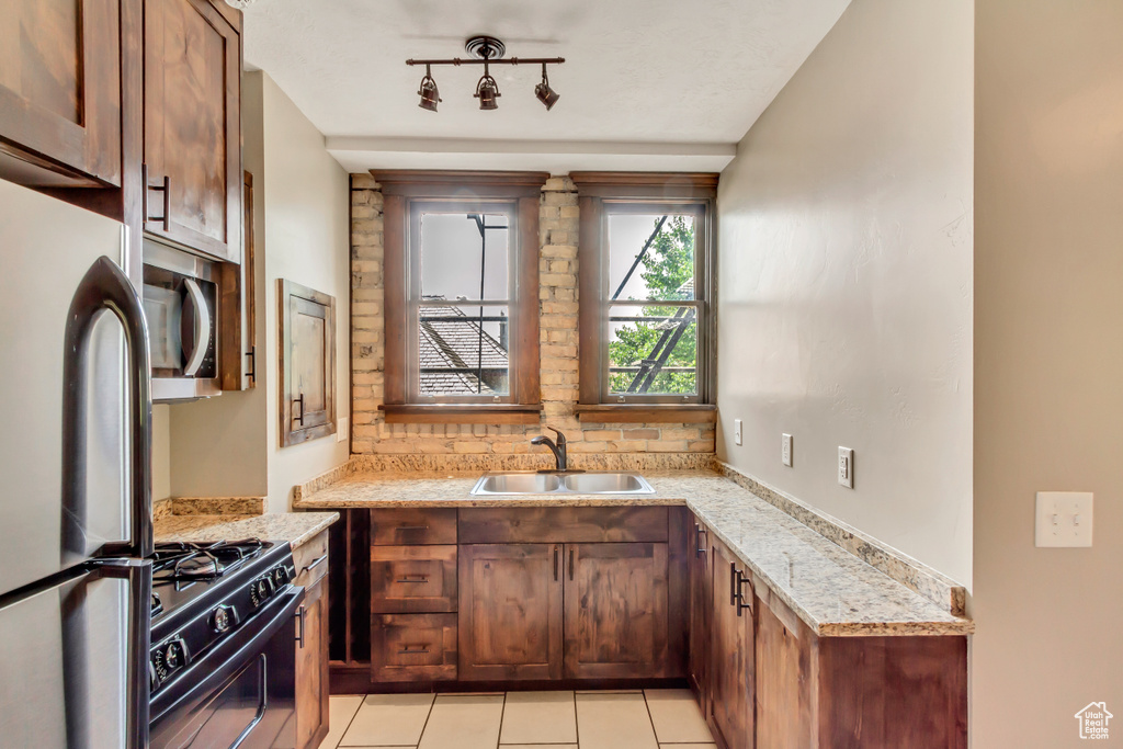 Kitchen with stainless steel appliances, rail lighting, sink, light stone countertops, and light tile patterned floors