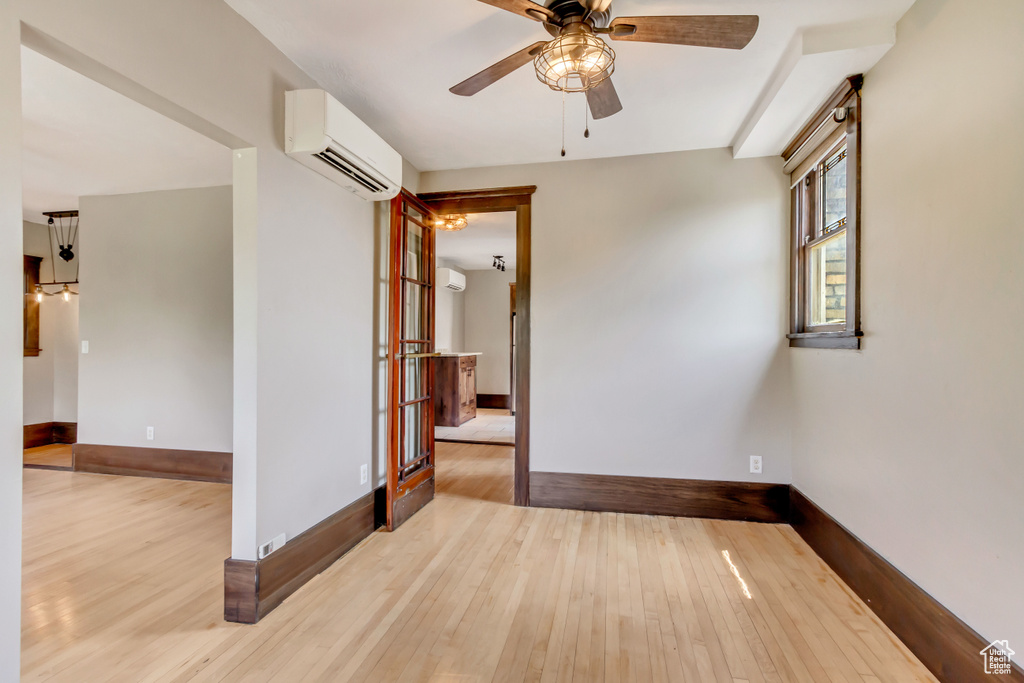 Unfurnished room featuring a wall mounted air conditioner, ceiling fan, and light hardwood / wood-style flooring