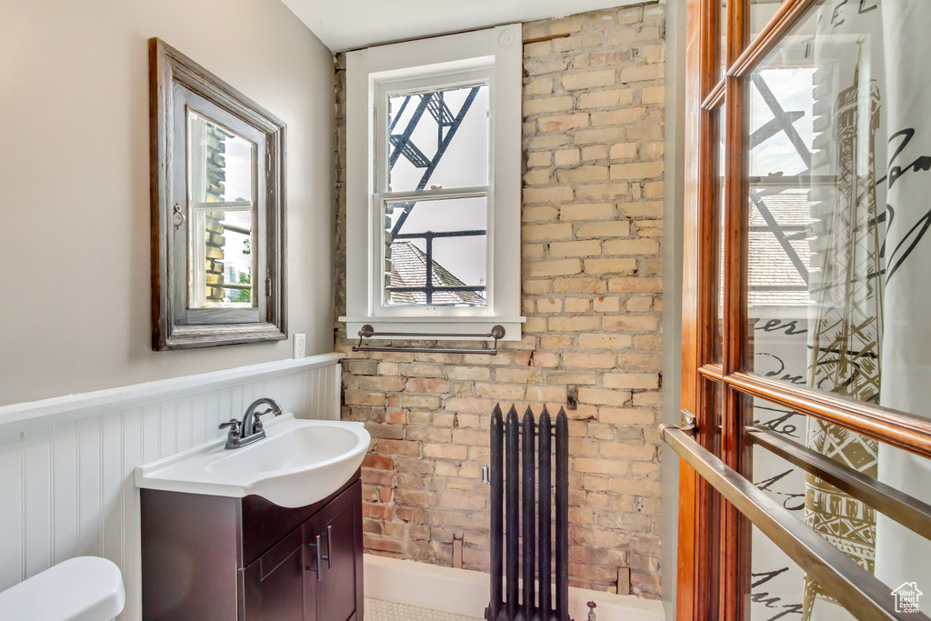 Bathroom featuring vanity, brick wall, radiator, and toilet