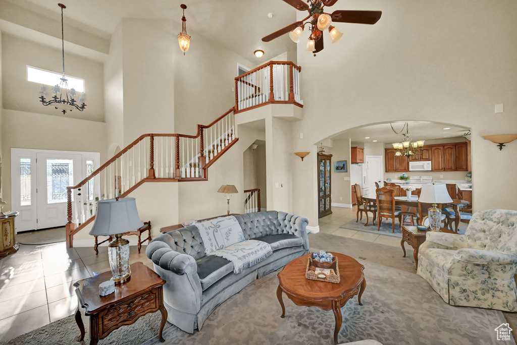 Living room with ceiling fan with notable chandelier, light tile patterned floors, and a high ceiling