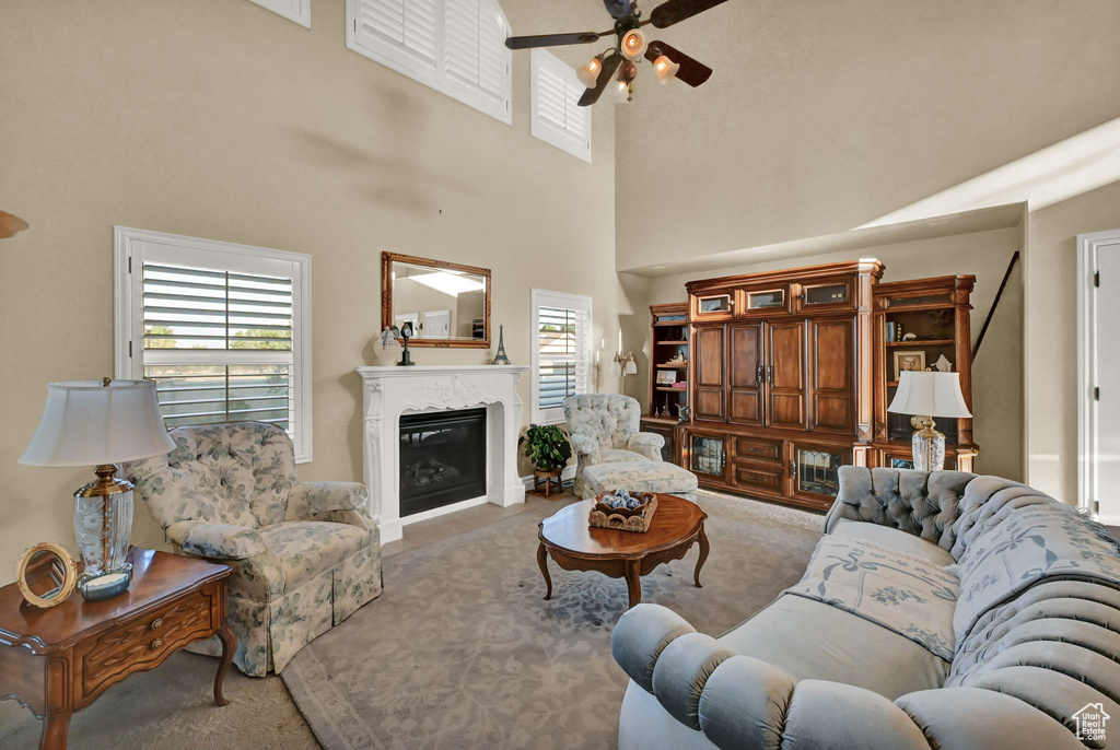 Carpeted living room featuring a high ceiling, a premium fireplace, and ceiling fan