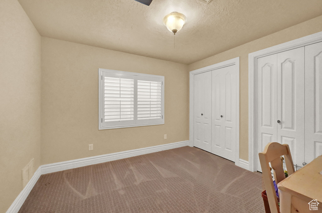 Unfurnished bedroom with carpet floors, multiple closets, and a textured ceiling