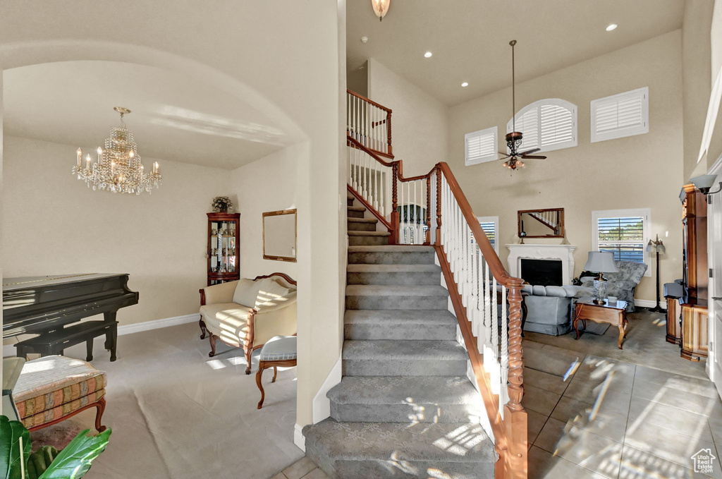 Stairway featuring light tile patterned flooring, ceiling fan with notable chandelier, and a high ceiling