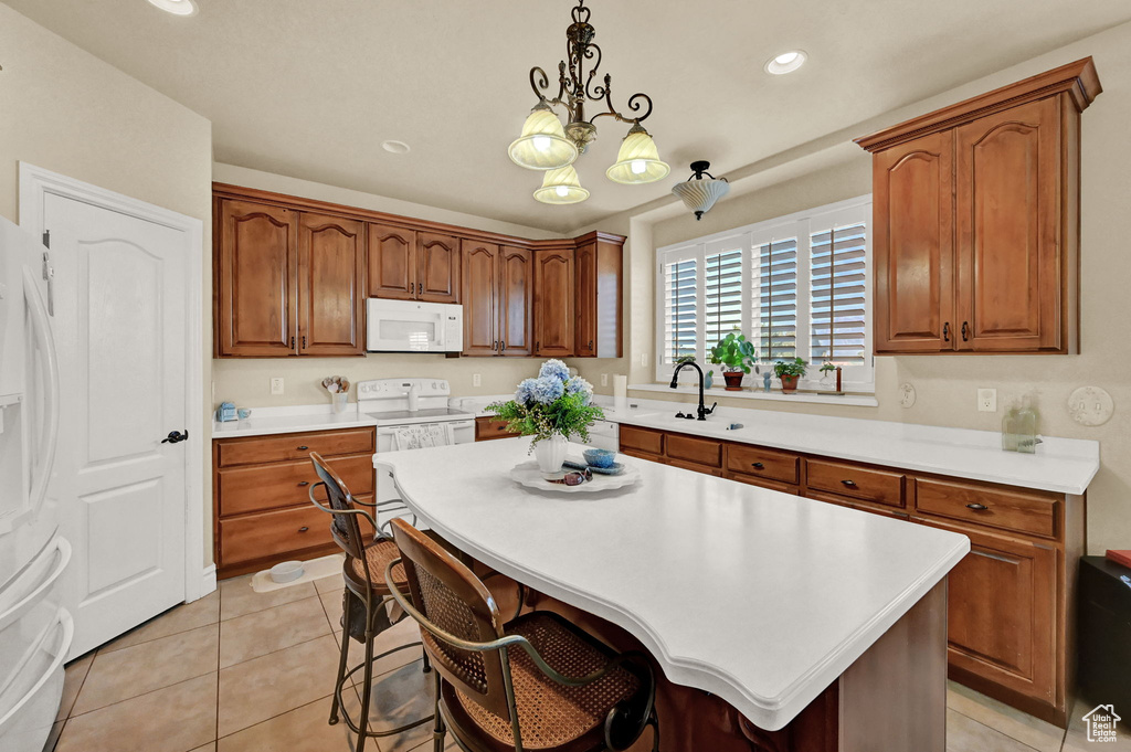 Kitchen with white appliances, an inviting chandelier, hanging light fixtures, light tile patterned floors, and a kitchen island