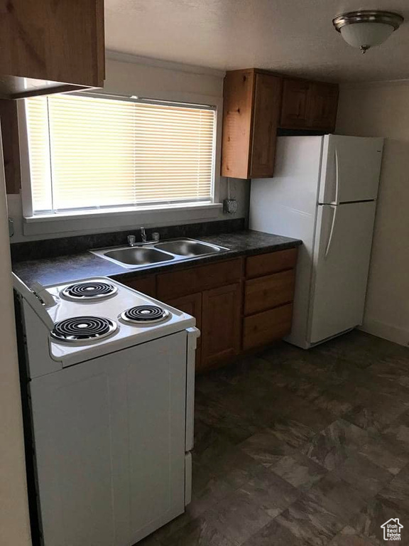 Kitchen with sink, dark tile patterned flooring, white appliances, and a healthy amount of sunlight