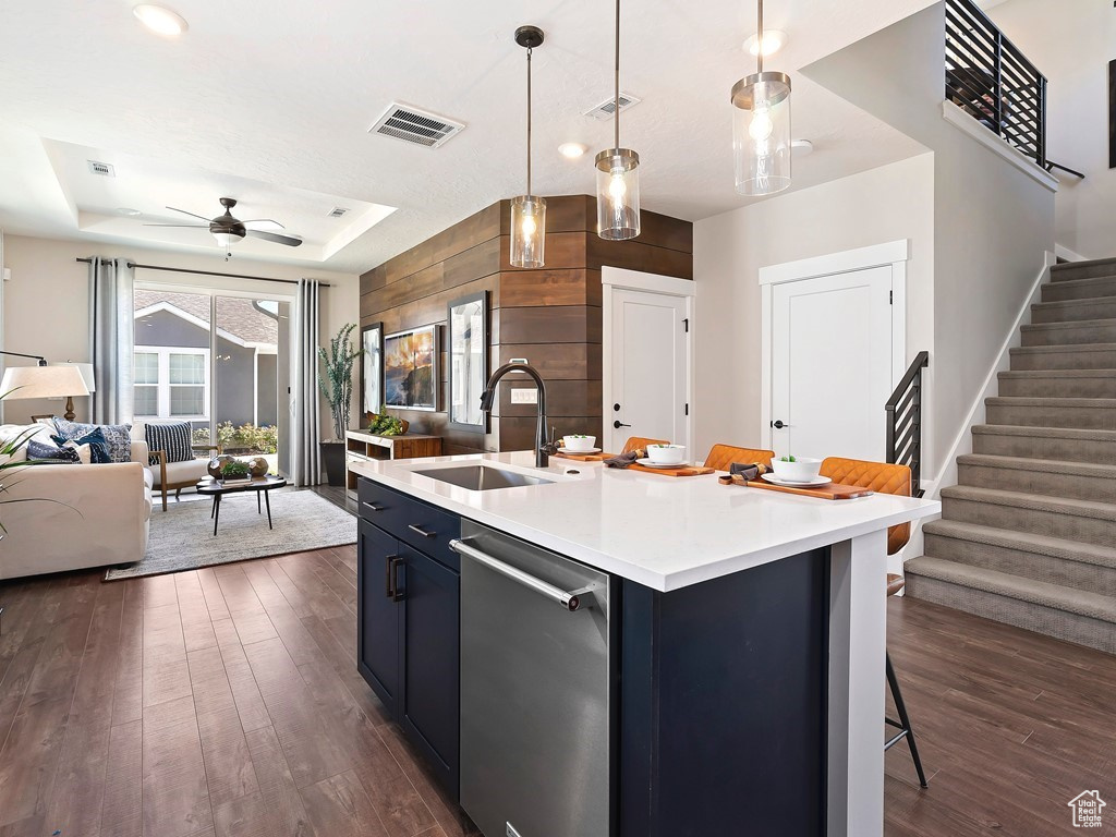 Kitchen with stainless steel dishwasher, dark hardwood / wood-style flooring, an island with sink, sink, and a raised ceiling