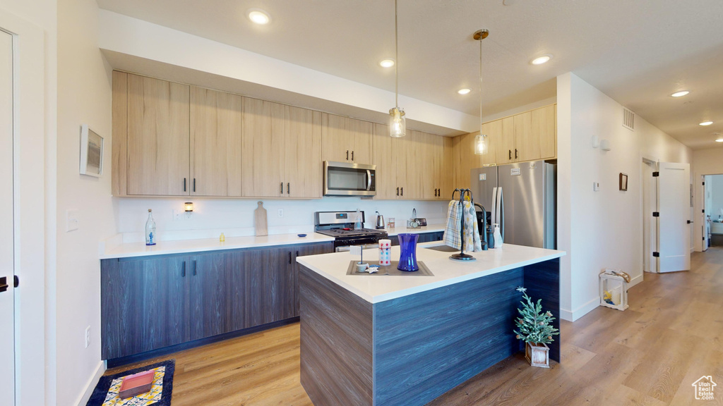 Kitchen with stainless steel appliances, pendant lighting, light brown cabinets, light hardwood / wood-style floors, and a center island