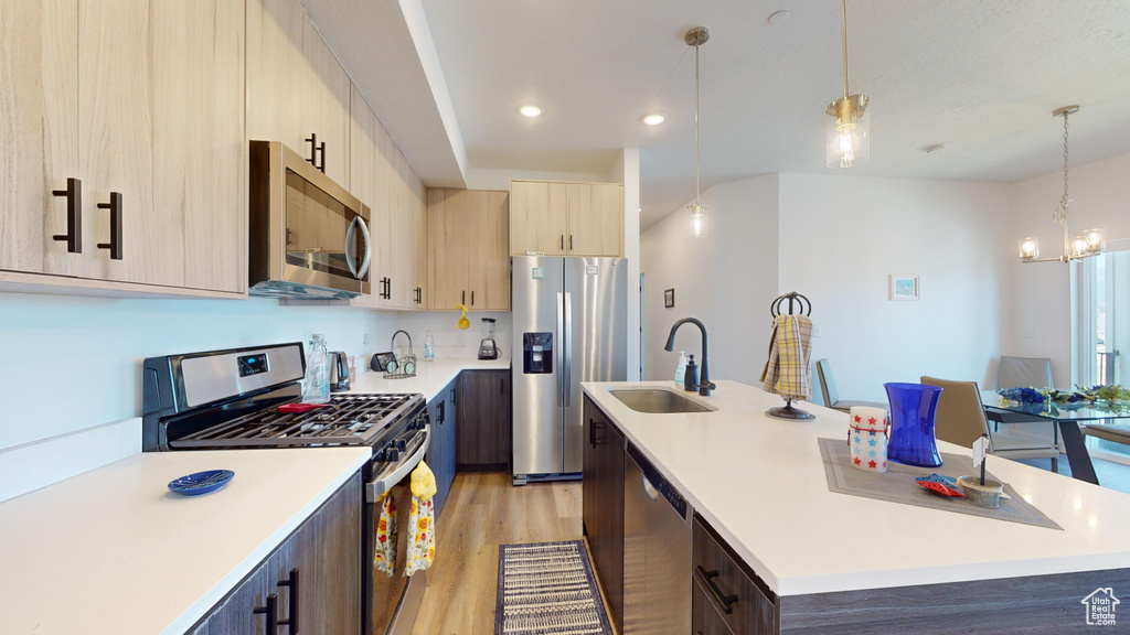 Kitchen featuring stainless steel appliances, a center island with sink, sink, pendant lighting, and light hardwood / wood-style floors