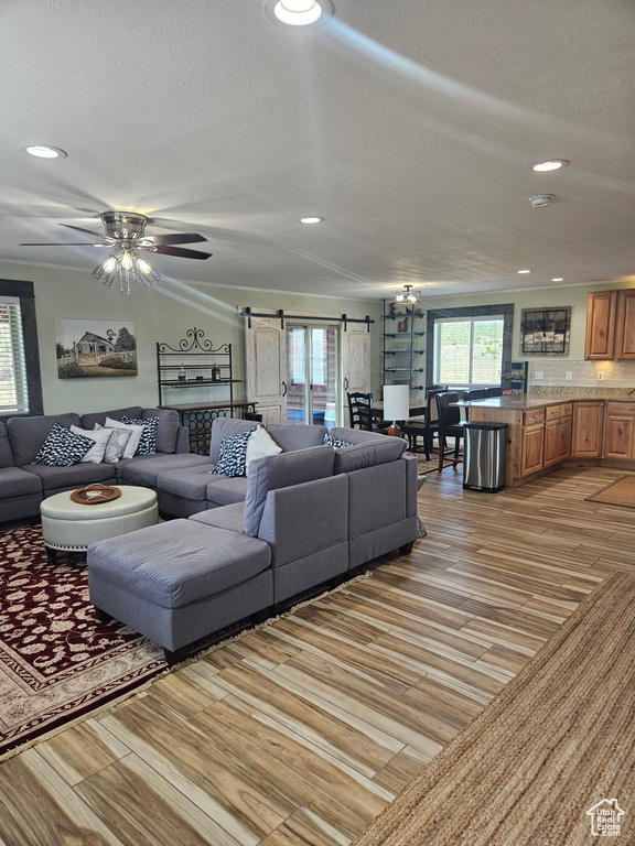 Living room featuring light hardwood / wood-style floors, a barn door, a textured ceiling, and ceiling fan