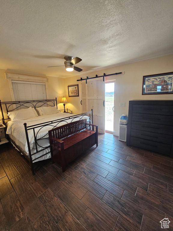 Bedroom featuring a barn door, access to outside, a textured ceiling, dark wood-type flooring, and ceiling fan