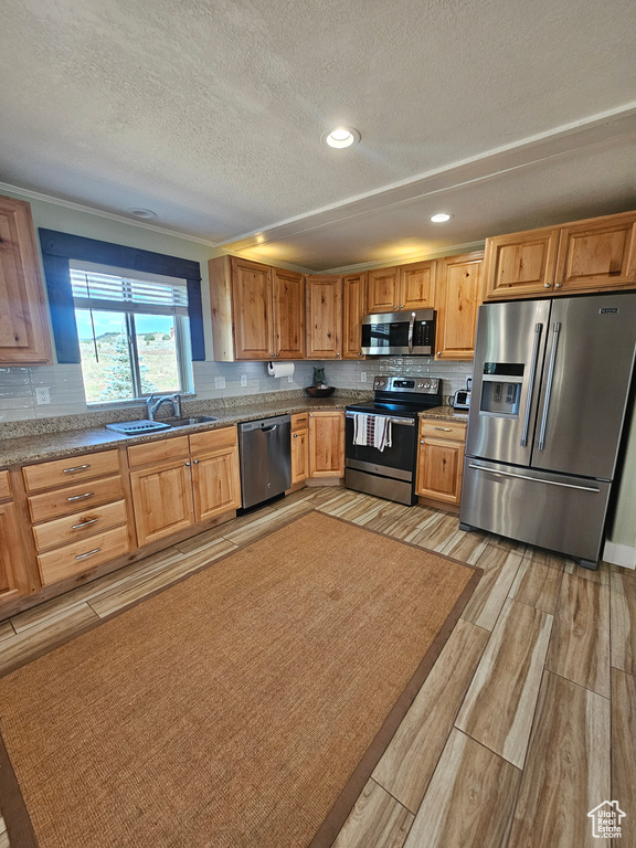 Kitchen with stone counters, stainless steel appliances, sink, backsplash, and a textured ceiling