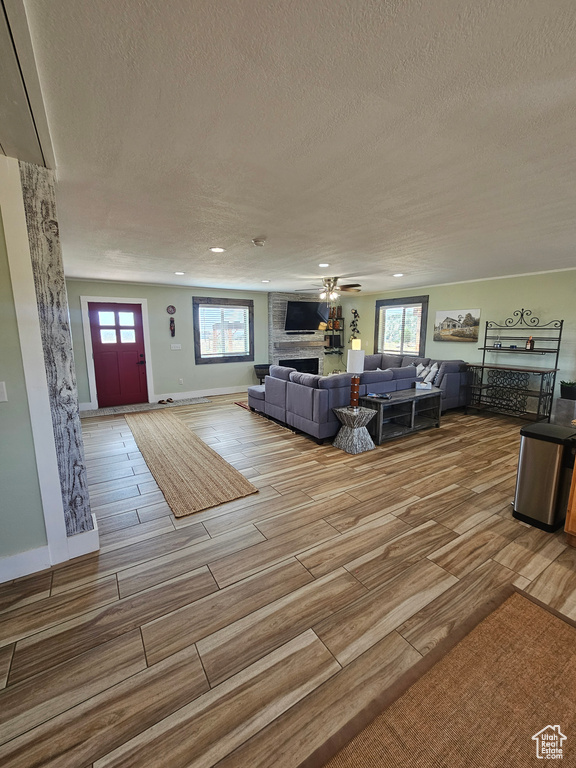 Unfurnished living room with a large fireplace, a textured ceiling, ceiling fan, and hardwood / wood-style floors