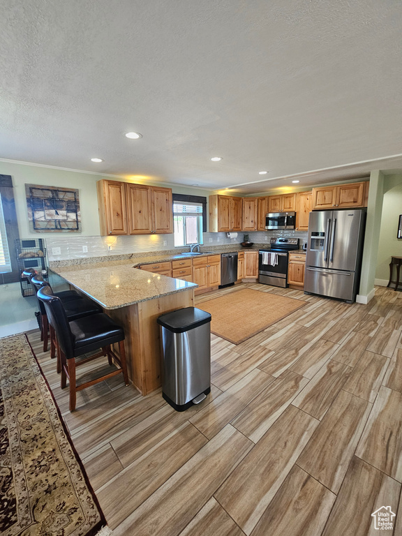 Kitchen featuring a breakfast bar, kitchen peninsula, stainless steel appliances, light stone countertops, and sink