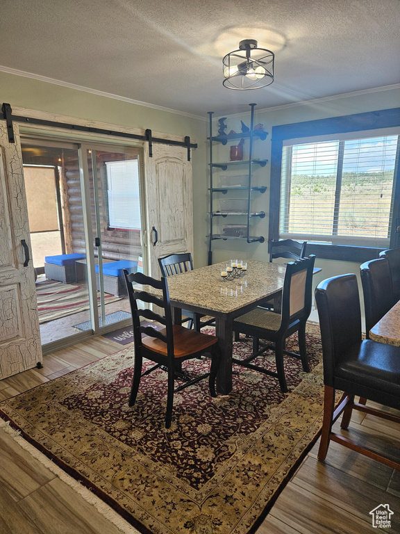 Dining room featuring a textured ceiling, a barn door, ceiling fan, hardwood / wood-style floors, and ornamental molding