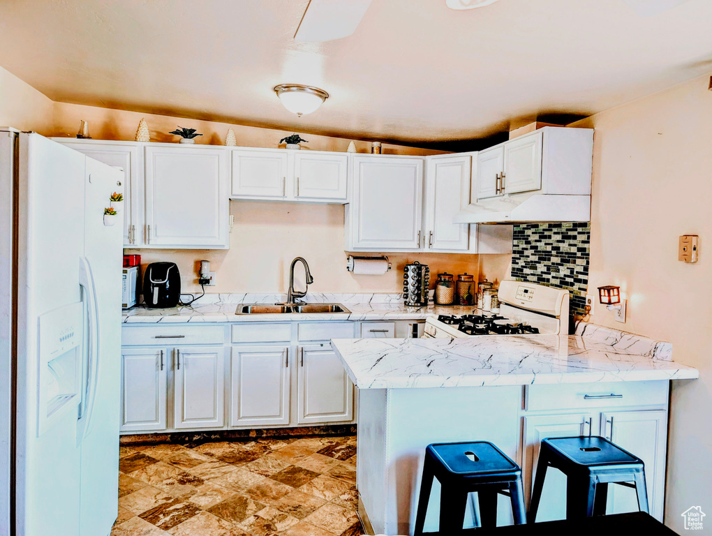 Kitchen featuring white appliances, light tile patterned floors, kitchen peninsula, sink, and a breakfast bar