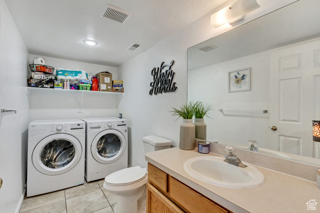 Washroom with light tile patterned flooring, washer and clothes dryer, and sink