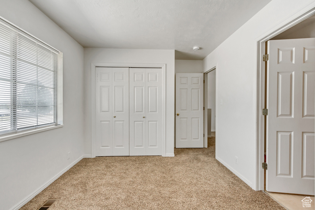 Unfurnished bedroom with light carpet, multiple windows, and a closet