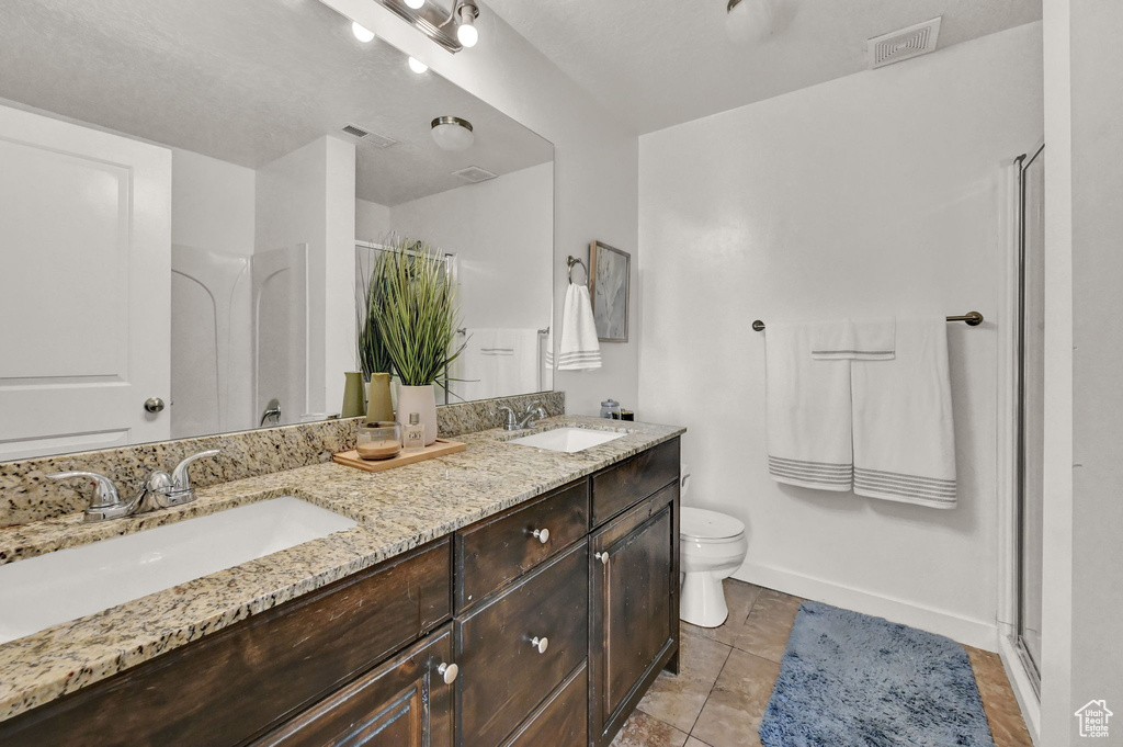 Bathroom featuring dual vanity, toilet, tile patterned floors, and walk in shower