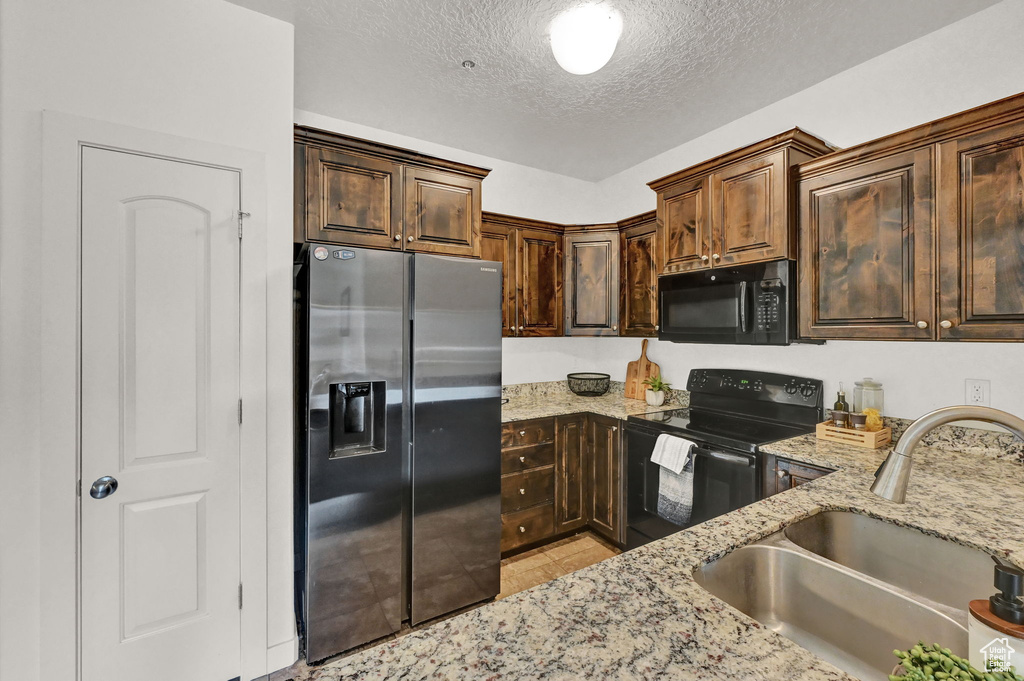 Kitchen with light tile patterned floors, a textured ceiling, black appliances, light stone countertops, and sink