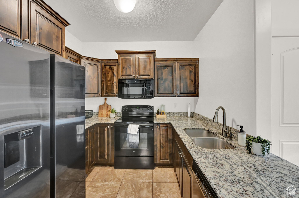 Kitchen with light tile patterned flooring, black appliances, sink, light stone countertops, and a textured ceiling