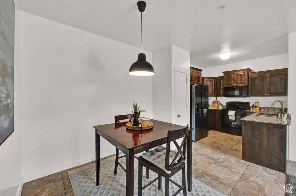 Kitchen with decorative light fixtures, black appliances, sink, dark brown cabinetry, and light tile patterned floors