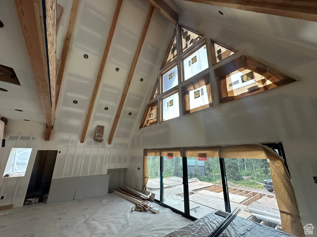 Unfurnished living room featuring high vaulted ceiling, a wealth of natural light, and beam ceiling