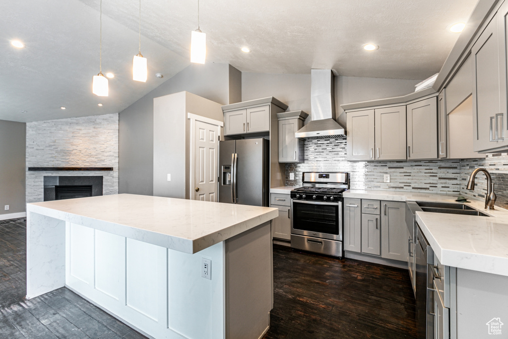 Kitchen featuring dark wood-type flooring, appliances with stainless steel finishes, a stone fireplace, and wall chimney exhaust hood