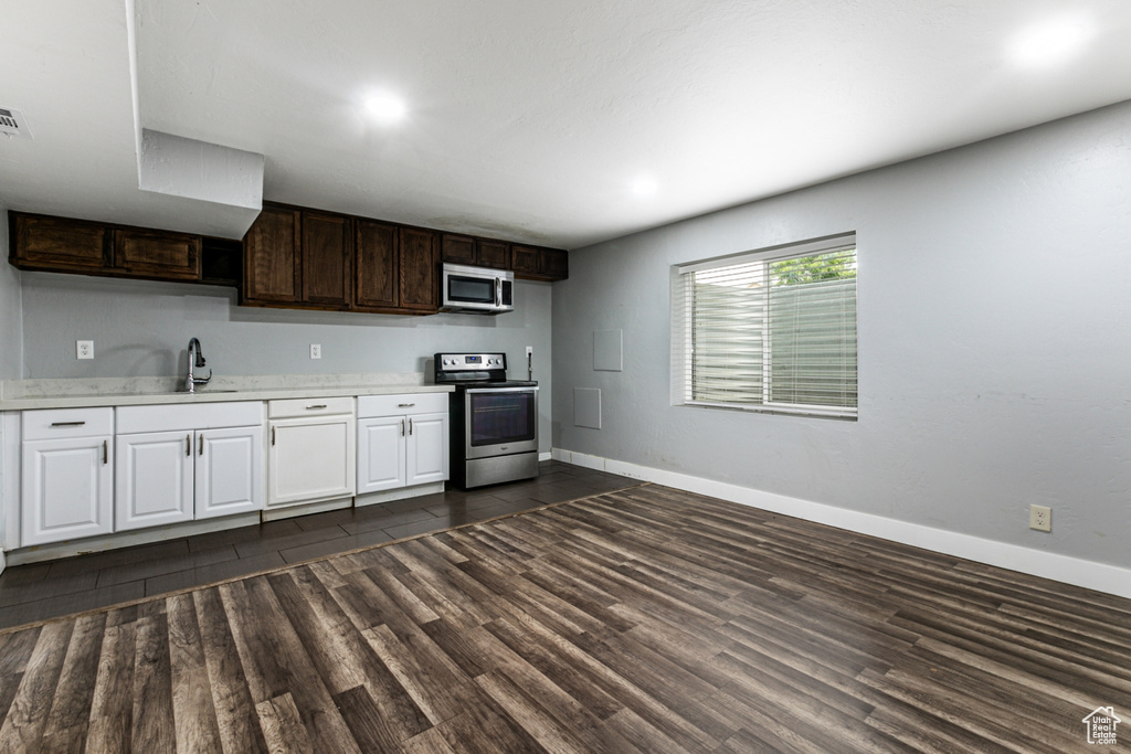 Kitchen featuring appliances with stainless steel finishes, sink, light stone counters, dark brown cabinetry, and dark hardwood / wood-style floors