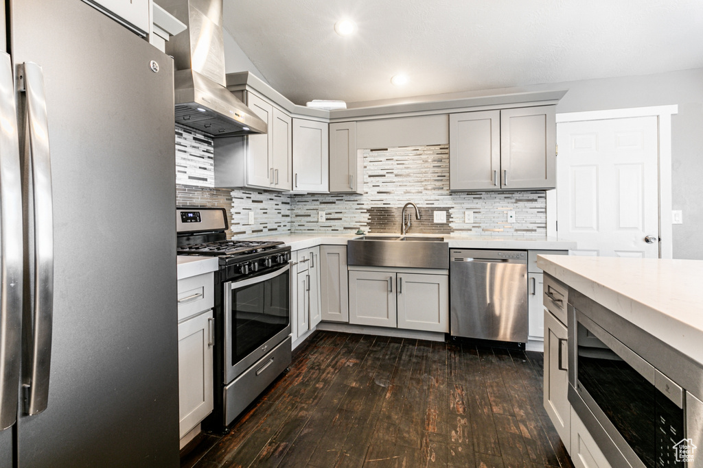 Kitchen with decorative backsplash, wall chimney exhaust hood, sink, appliances with stainless steel finishes, and dark wood-type flooring