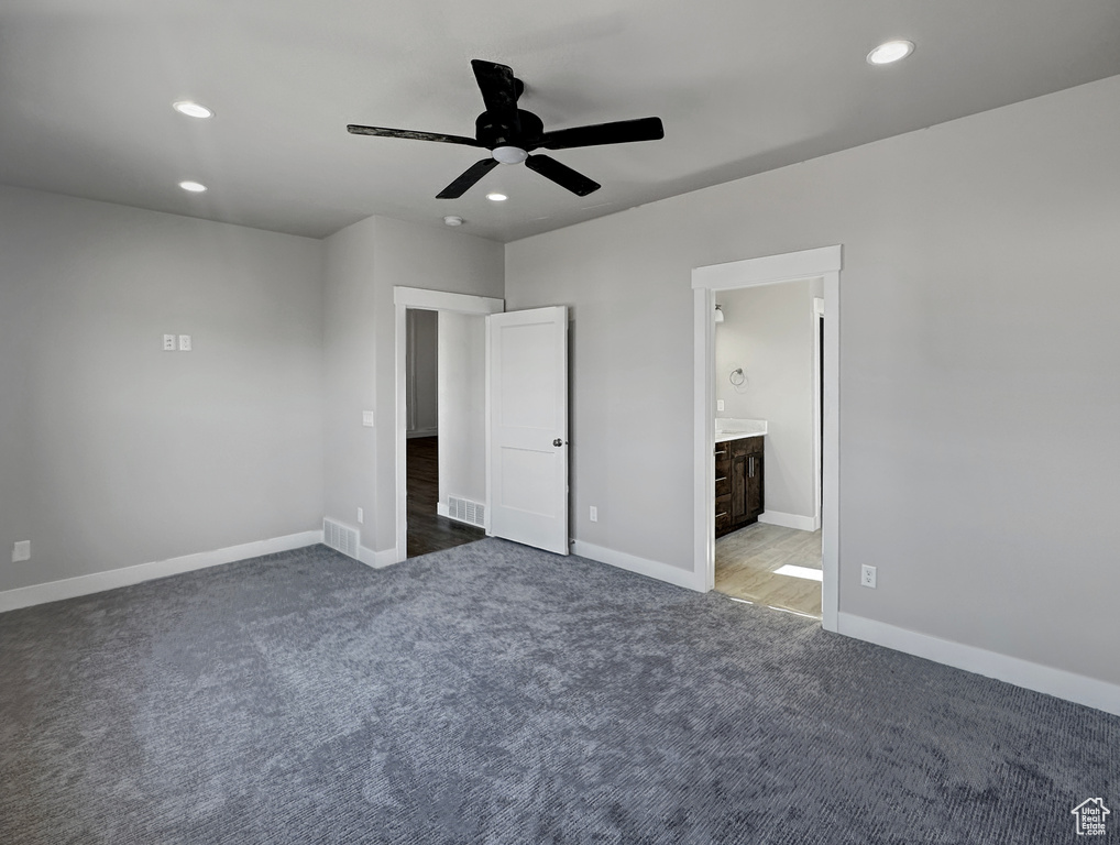 Unfurnished bedroom featuring ceiling fan, ensuite bathroom, and dark carpet