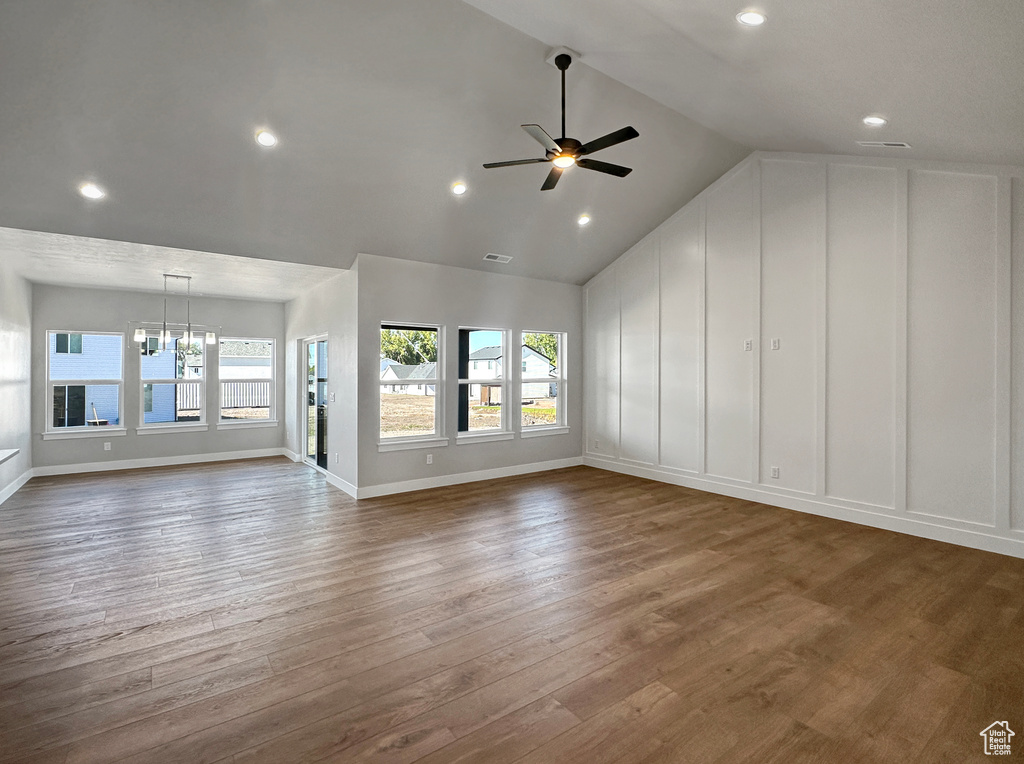 Unfurnished living room featuring ceiling fan with notable chandelier, vaulted ceiling, and dark hardwood / wood-style floors