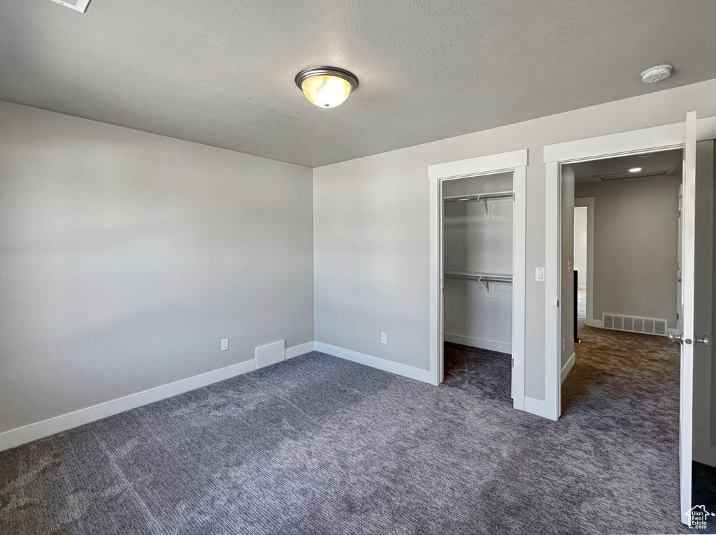 Unfurnished bedroom with dark carpet, a textured ceiling, and a closet